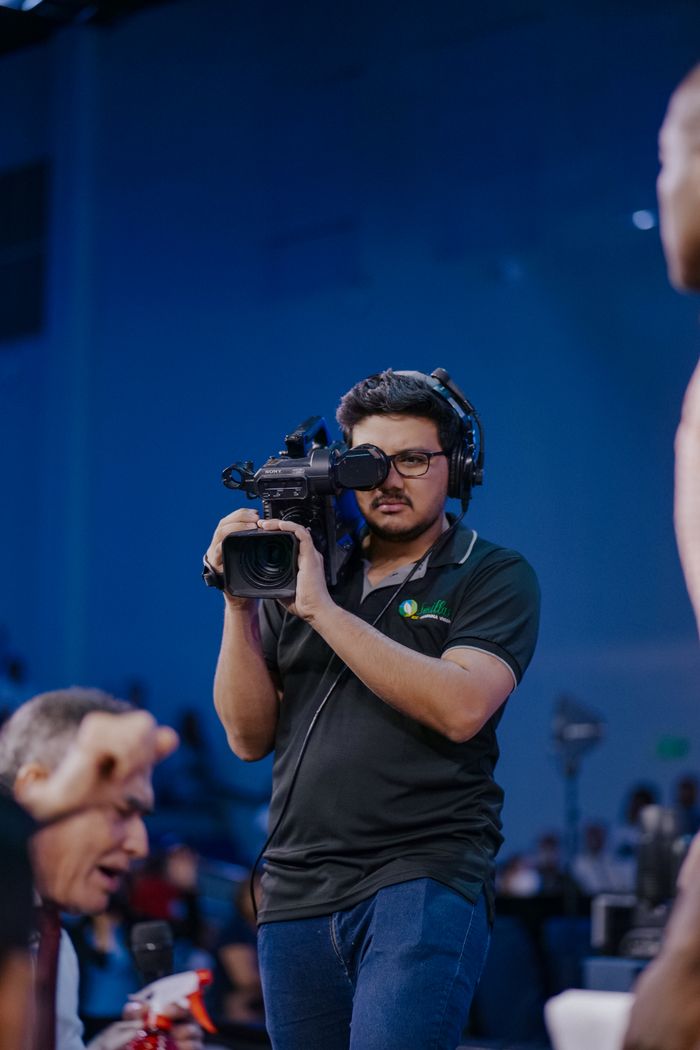 Cameraman in action filming an event with eyeglasses and headphones.