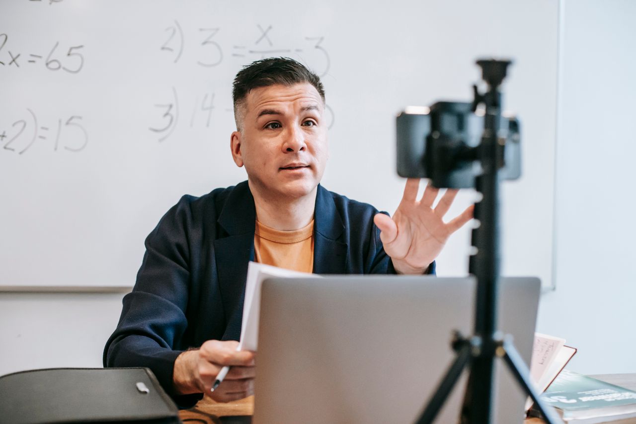 A male instructor conducting an online teaching session using a laptop and camera setup.