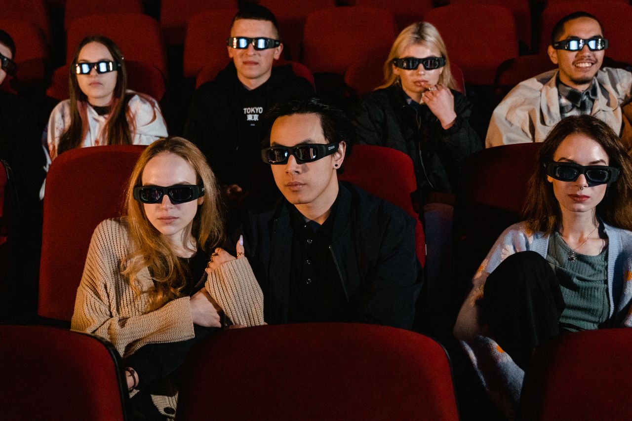 A diverse group of people wearing 3D glasses watch a movie in a theater.